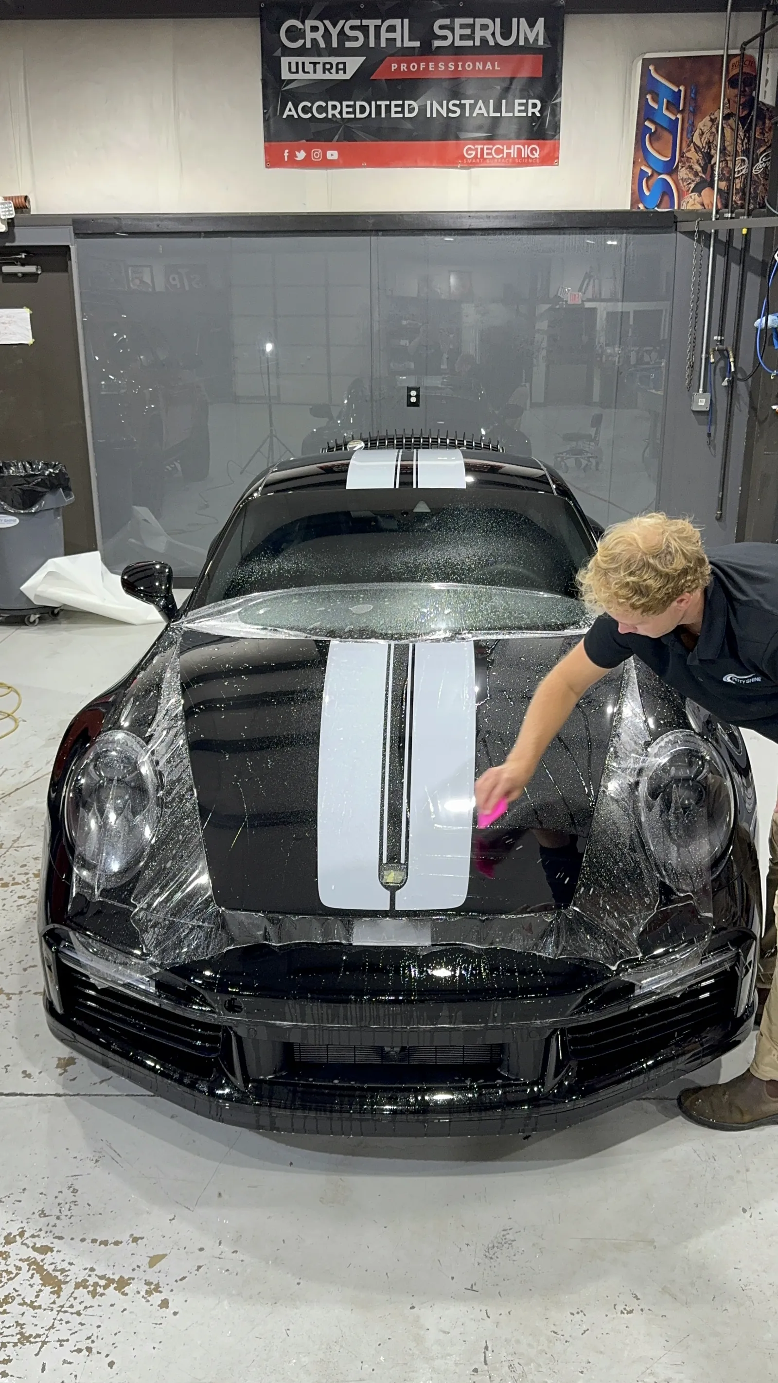 Paint protection film being applied to the hood of a black Porsche 911 with a white stripe at Petty Shine